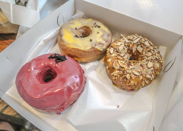 Three donuts in a box: a strawberry cream, lemon cream and a donut covered in almond flakes.